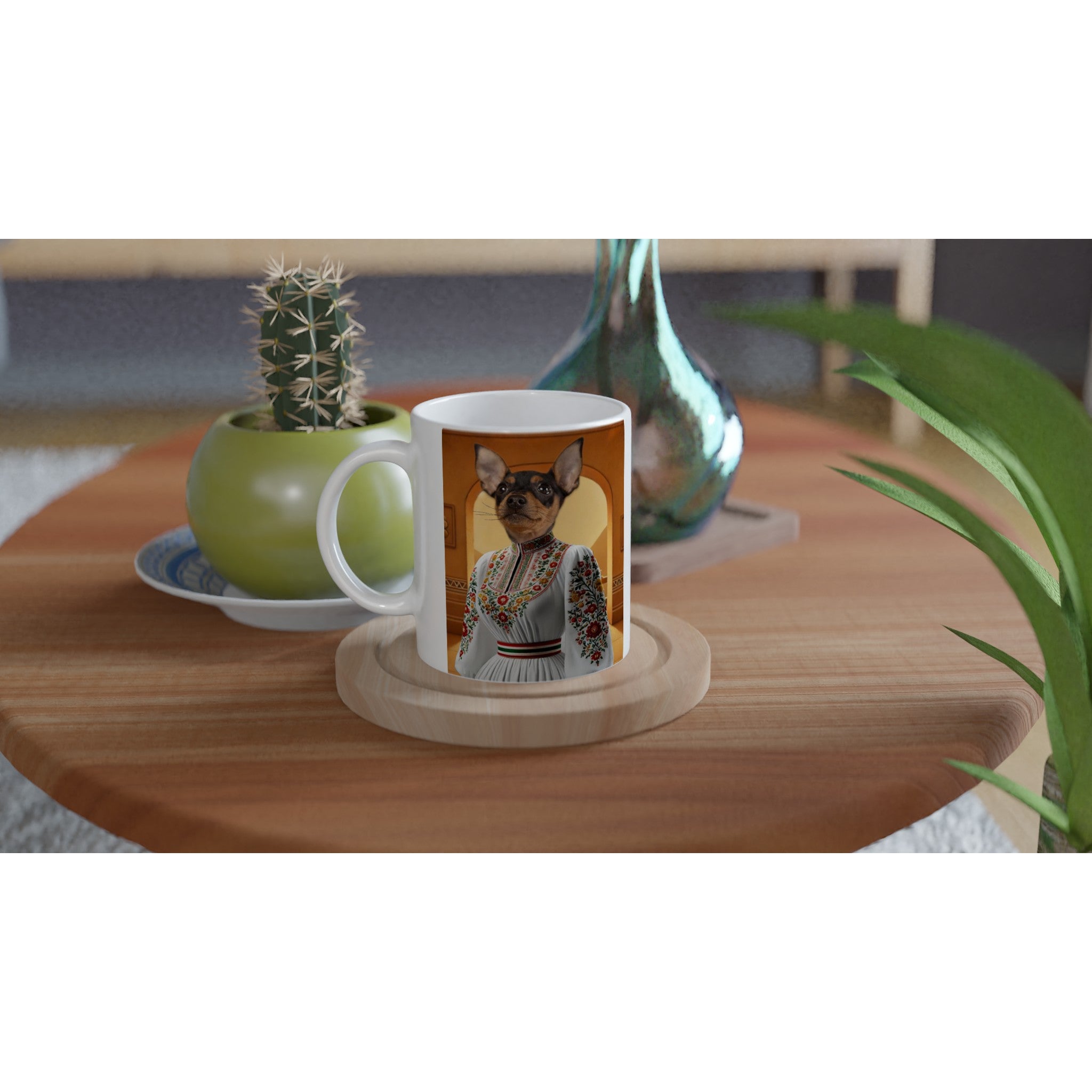 Mug blanc personnalisé posé sur une table en bois, imprimé d’un portrait stylisé d’un petit chien pinscher miniature vêtu d’une robe traditionnelle blanche brodée de motifs floraux, à côté d’un cactus en pot vert et d’un vase en céramique bleutée.