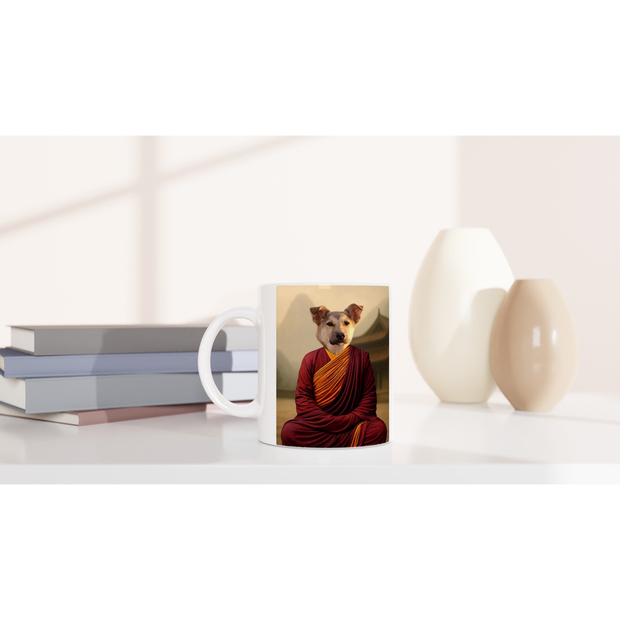Mug blanc posé sur un bureau épuré, imprimé d’un chien en robe de moine bouddhiste rouge et safran en posture de méditation, entouré de livres empilés à gauche et de deux vases beiges à droite.