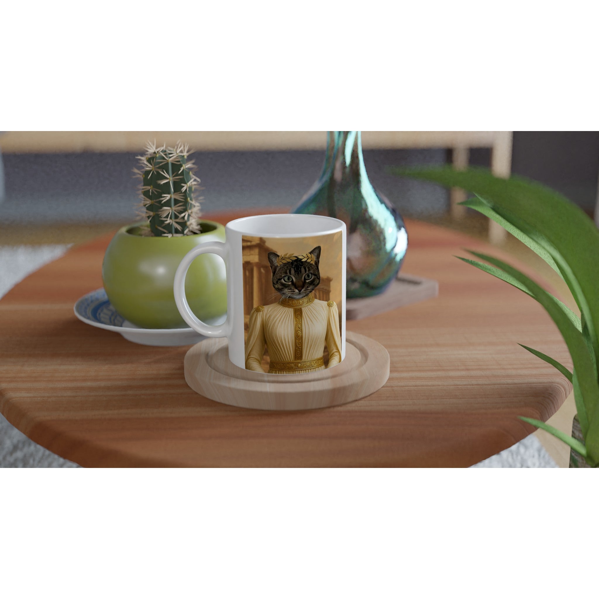 Mug blanc personnalisé affichant un portrait de chat en costume impérial doré, posé sur une table en bois ronde à côté d’un petit cactus en pot vert et d’un vase décoratif.