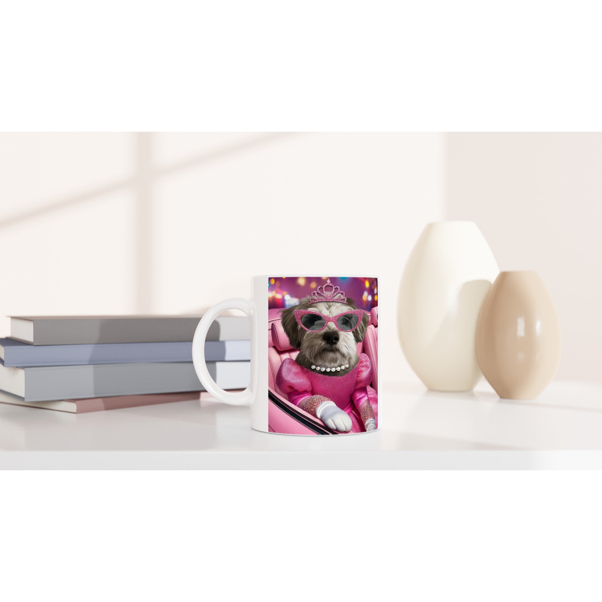 Mug blanc posé sur une table minimaliste, illustré d’un petit chien habillé en princesse rose (robe scintillante, diadème, collier de perles et lunettes de soleil) avec en arrière-plan des livres empilés et des vases décoratifs.