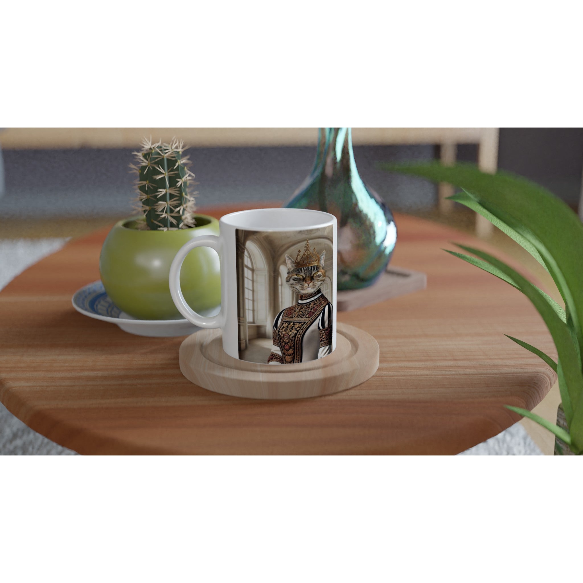 Mug blanc sur table en bois, illustré d’un chat couronné en tenue renaissance, posé sur un sous-verre en bois à côté d’un cactus et d’un vase coloré.