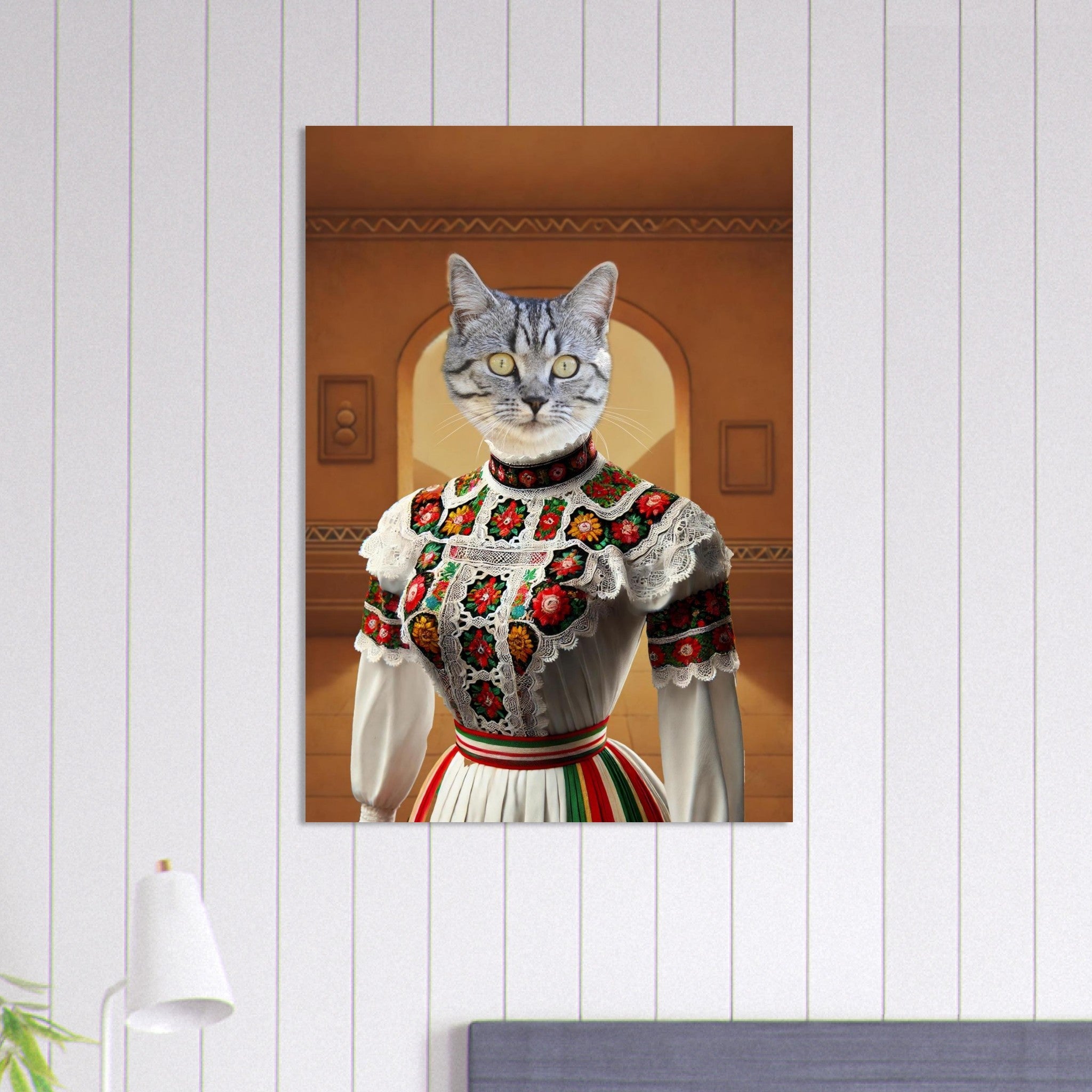 Portrait d’un chat gris anthropomorphe vêtu d’une robe folklorique blanche ornée de dentelle et de broderies rouges et vertes, posé devant un mur ocre avec une arcade.