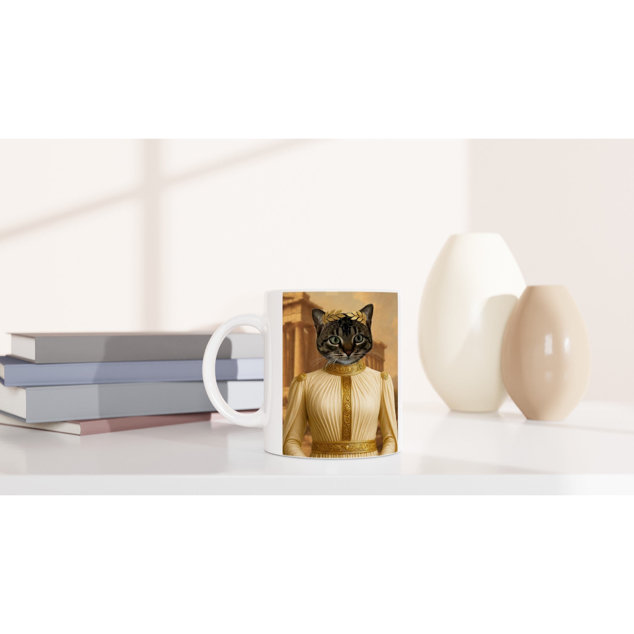 Mug blanc imprimé d’un chat à tête de tabby vêtu d’une toge blanche et dorée avec couronne de laurier, posé sur un meuble épuré aux côtés de livres empilés et de vases décoratifs