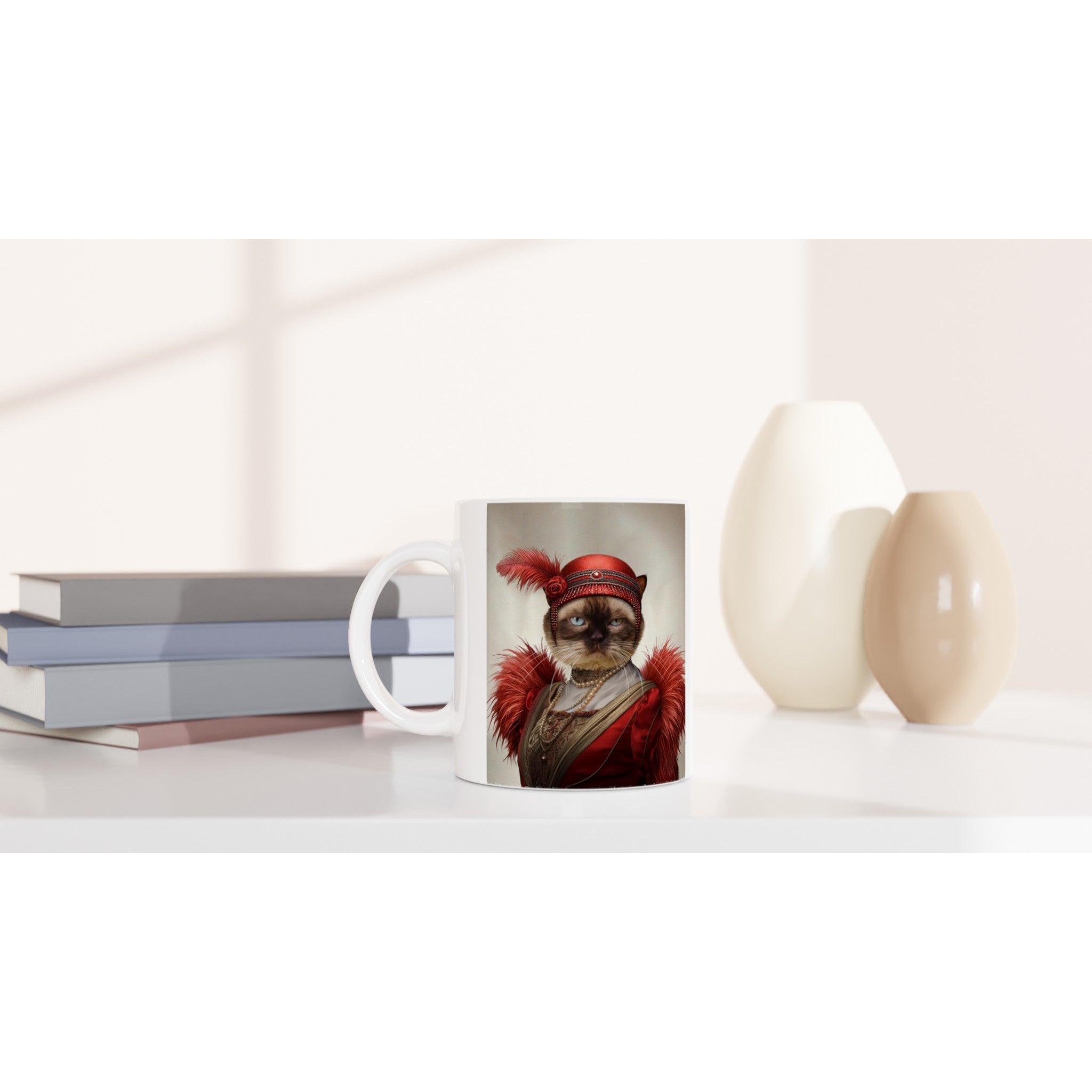 Tasse blanche posée sur un bureau, imprimée d’un chat au regard impassible vêtu d’un costume et d’un chapeau rouge orné de plumes, à côté d’une pile de livres et de deux vases beiges.