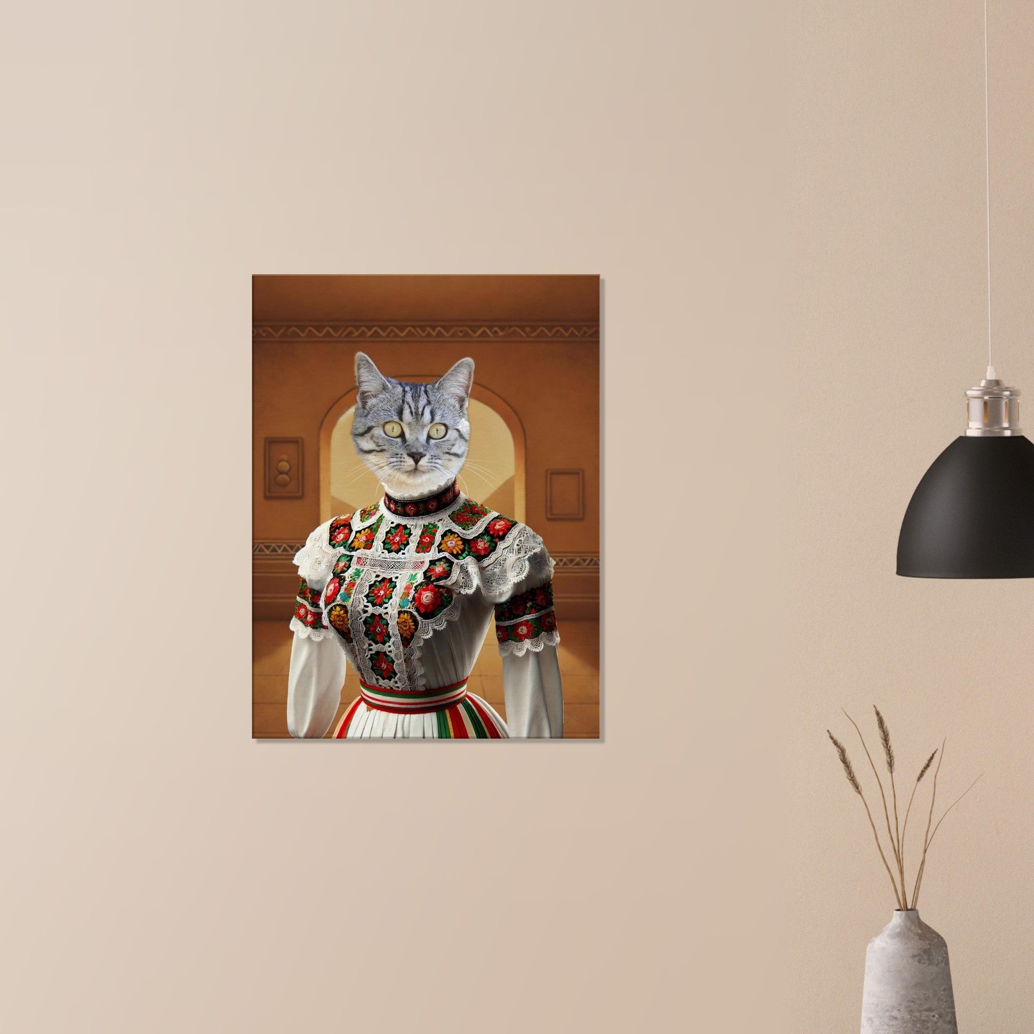 Portrait mural surréaliste d’un chat gris au buste humain vêtu d’une robe folklorique blanche richement brodée de fleurs rouges et vertes, accroché sur un mur beige avec une lampe noire et un vase en céramique.