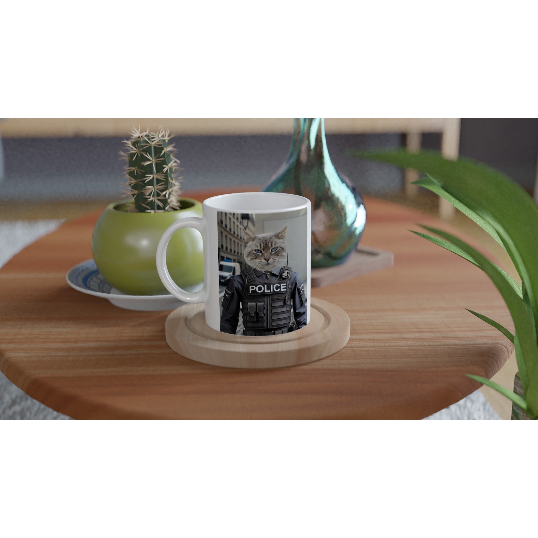 Tasse blanche posée sur une table basse en bois, imprimée d’un chat en uniforme de police, entourée d’un petit cactus en pot vert et d’un vase décoratif.