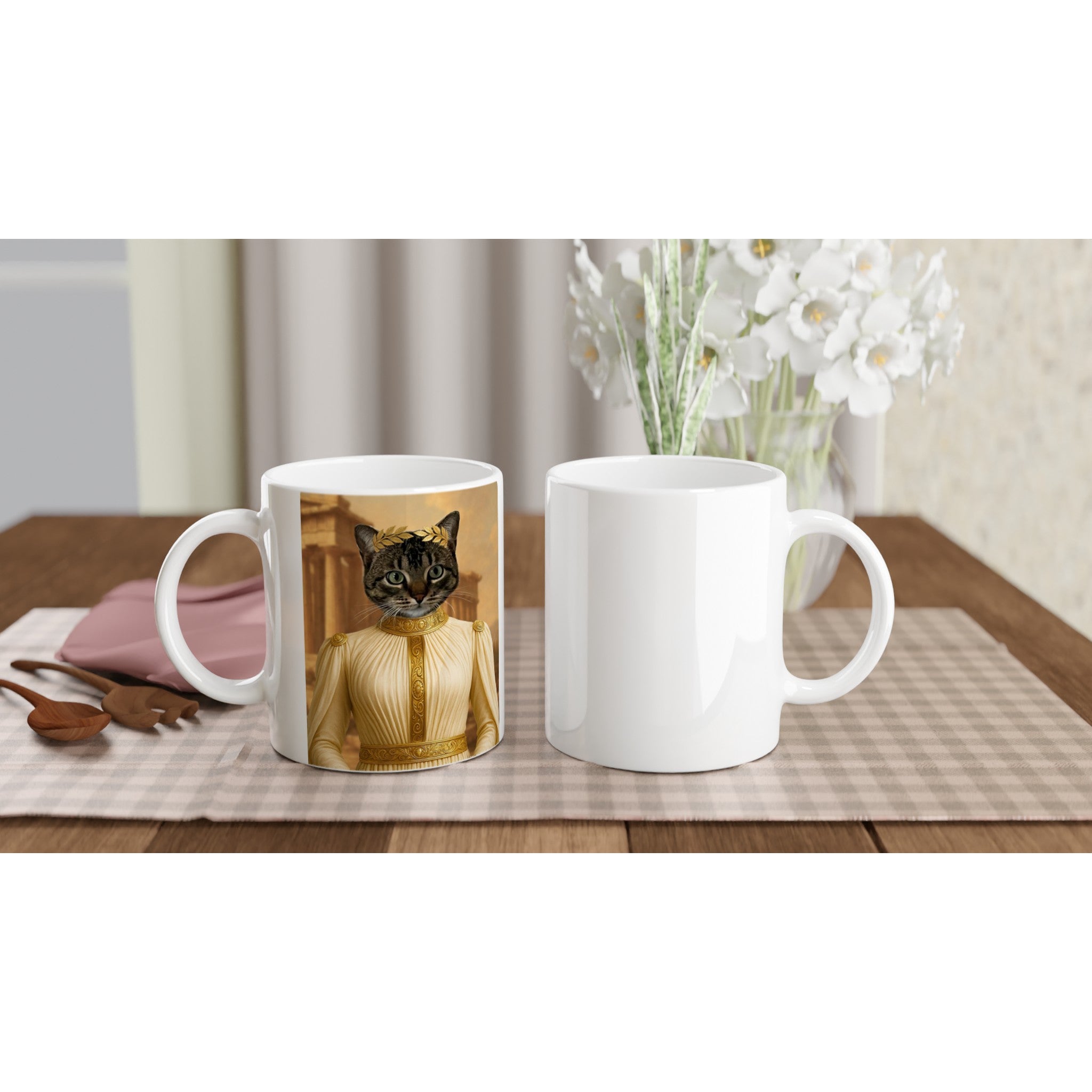 Mug blanc imprimé d’un chat en toge romaine dorée avec couronne de laurier, posé à côté d’un second mug vierge sur une nappe à carreaux, cuillères en bois et bouquet de fleurs blanches en arrière-plan.