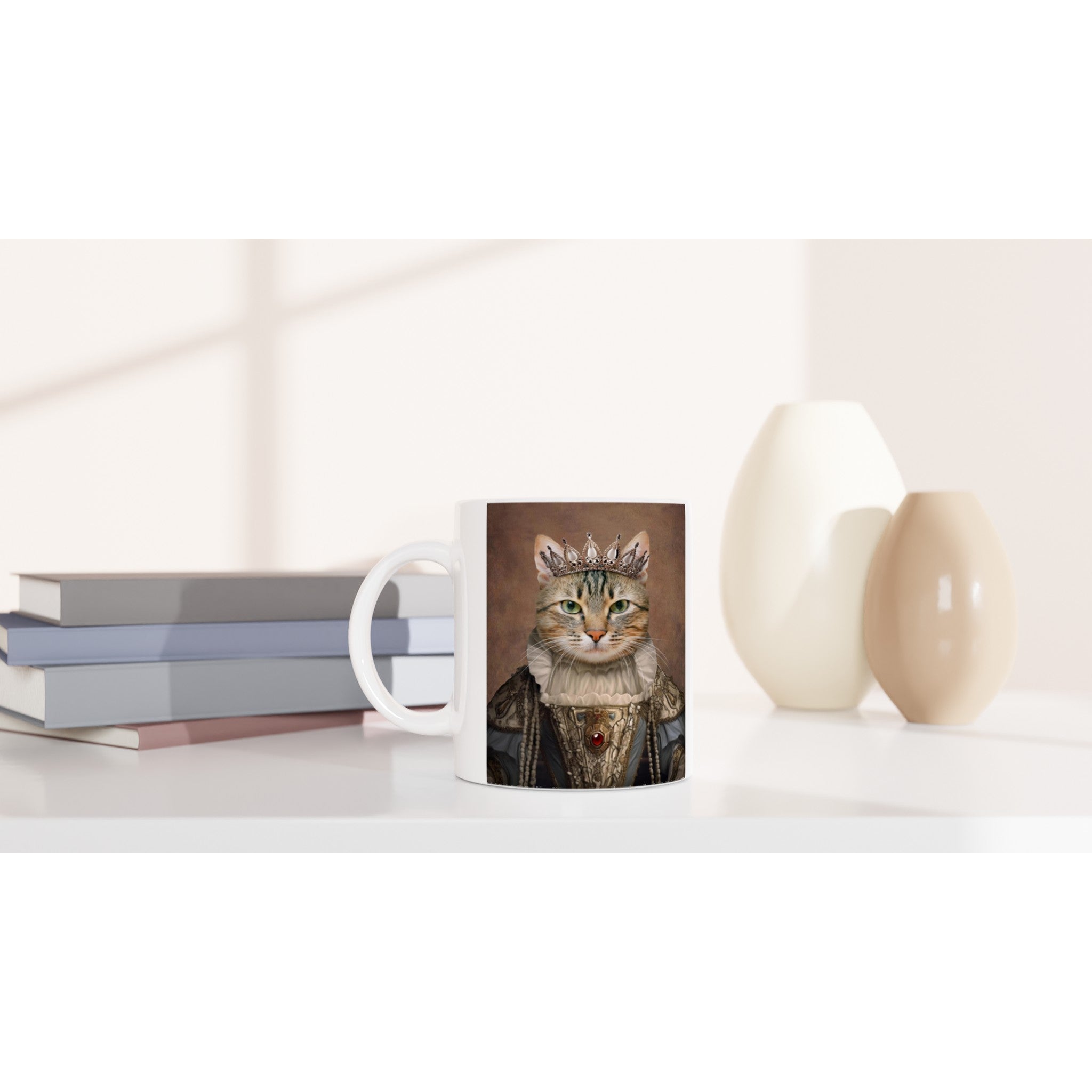 mug blanc personnalisé avec un chat portant une couronne et un costume Renaissance royal, posé sur une table blanche à côté de livres empilés et de vases décoratifs moderne