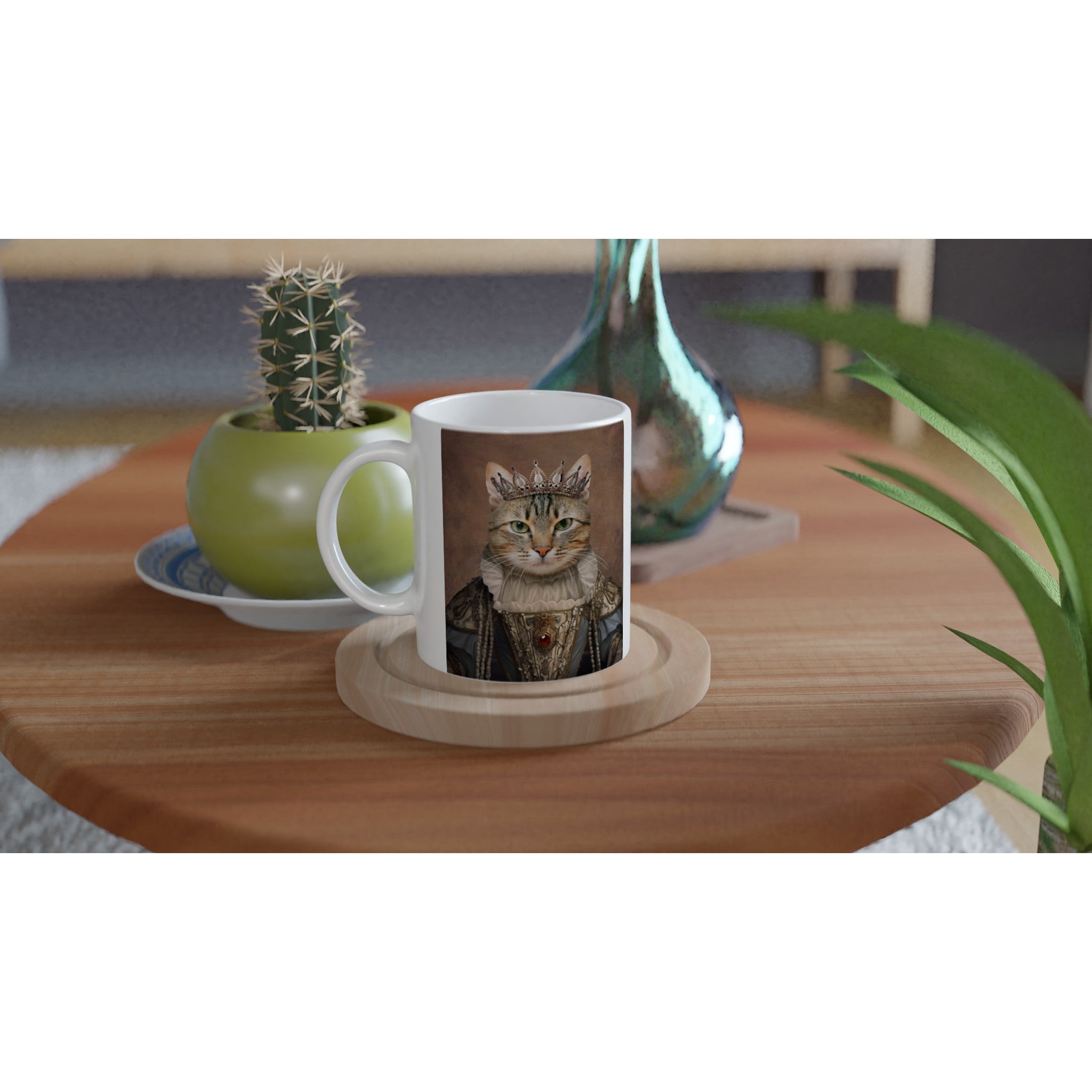 Mug blanc sur table en bois, imprimé d’un chat couronné en costume royal, posé à côté d’un cactus en pot et d’une plante verte décorative.